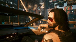 A screenshot from Cyberpunk 2077's 2.2 update showing Johnny Silverhand riding through Night City in the passenger seat of a convertible car.